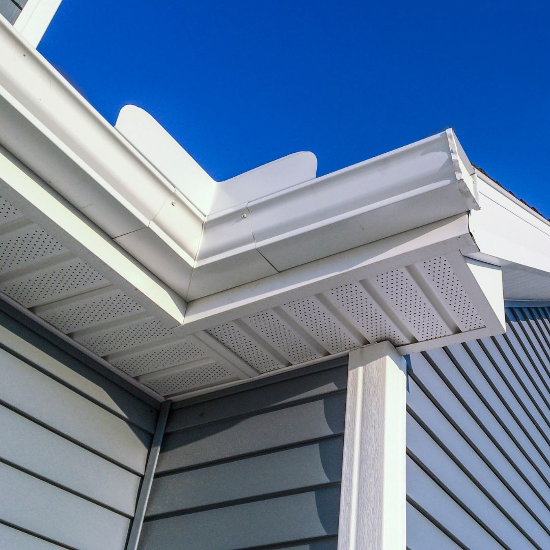 Close-up of a white gutter and roof edge on a house, with a bright blue sky in the background.